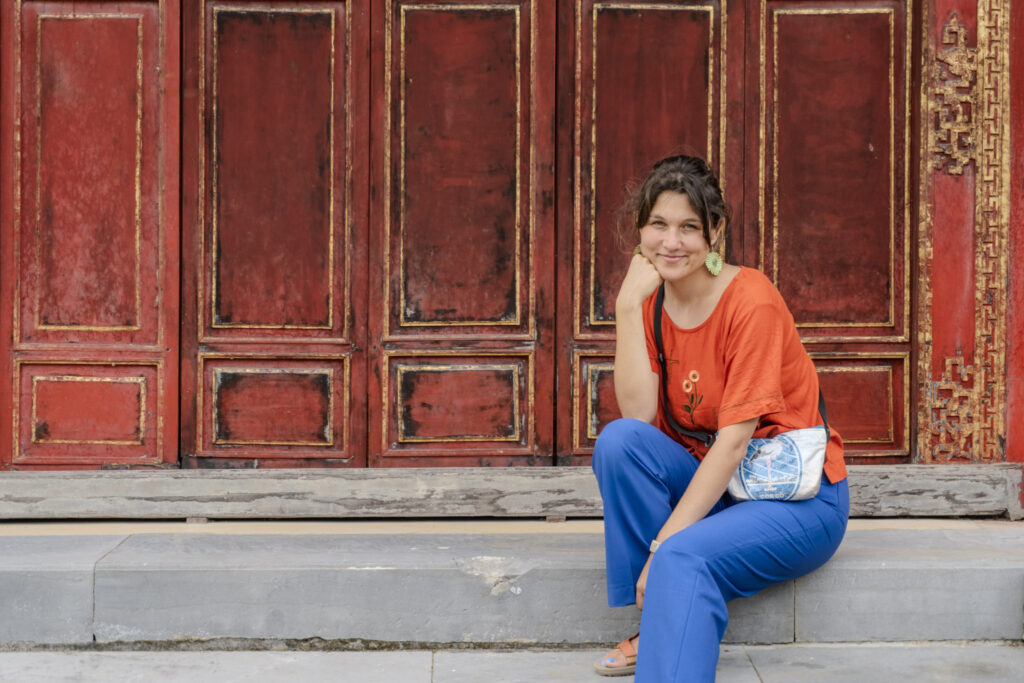 Veronica Voltolini creatrice di Nuances, seduta davanti a una porta rossa e oro, Vietnam